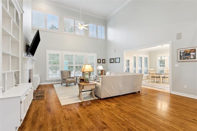 living room with hardwood / wood-style flooring, ceiling fan, crown molding, and a high ceiling