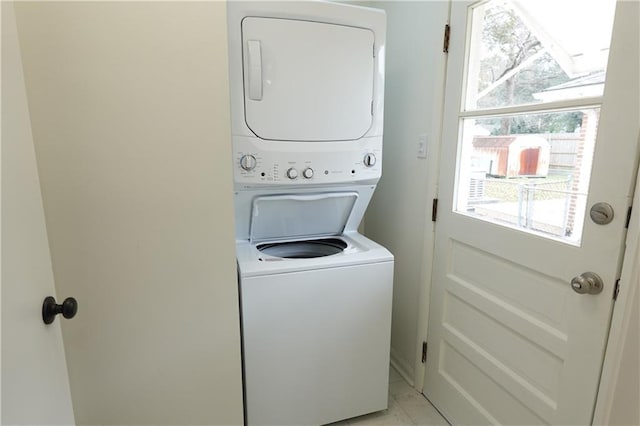 washroom featuring light tile patterned floors, stacked washer and dryer, and a wealth of natural light