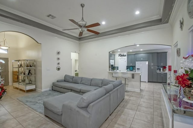 tiled living room with a high ceiling, a raised ceiling, ceiling fan, and ornamental molding