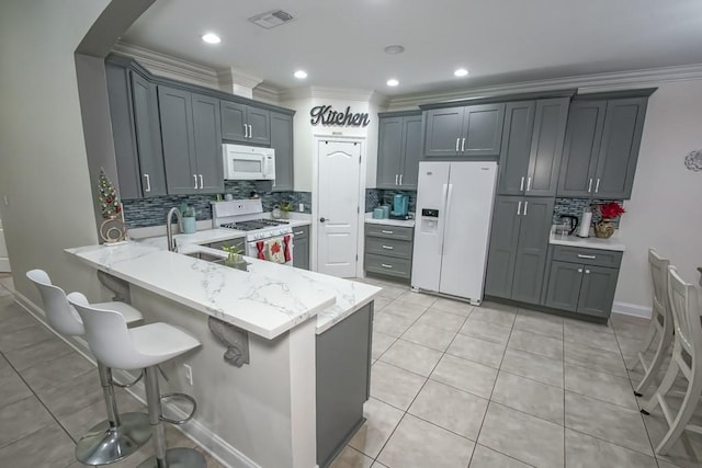 kitchen with kitchen peninsula, ornamental molding, white appliances, and gray cabinetry