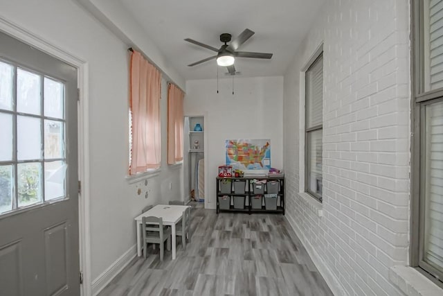 doorway to outside featuring ceiling fan, light wood-type flooring, and brick wall