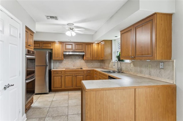 kitchen featuring sink, backsplash, kitchen peninsula, light tile patterned flooring, and appliances with stainless steel finishes