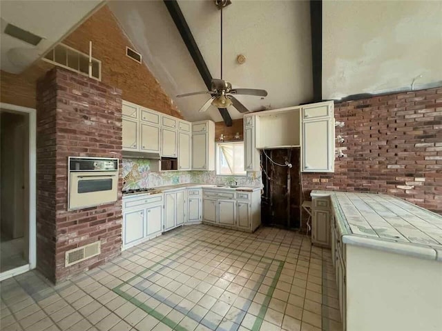 kitchen with white oven, beamed ceiling, brick wall, tile countertops, and light tile patterned flooring