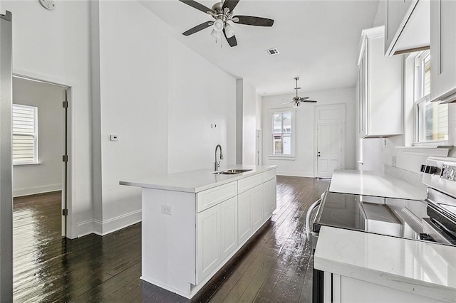 kitchen with white cabinets, light countertops, a center island with sink, and visible vents