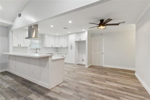 kitchen featuring kitchen peninsula, light hardwood / wood-style floors, island exhaust hood, white cabinets, and ceiling fan