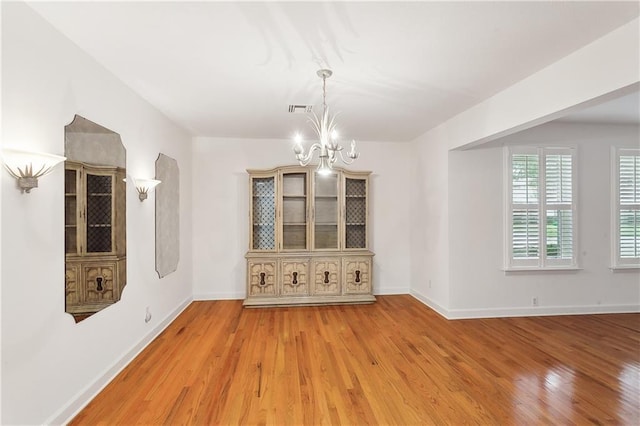 unfurnished dining area with wood-type flooring and a notable chandelier