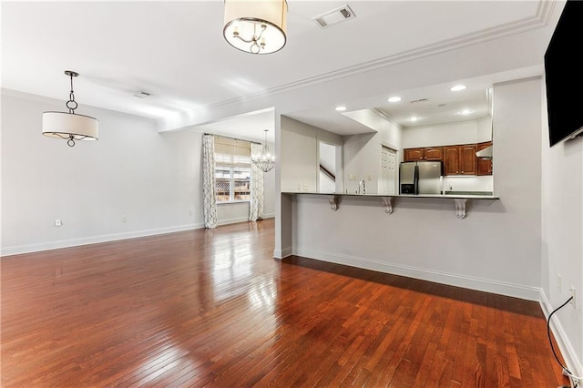 kitchen with dark wood-type flooring, stainless steel refrigerator with ice dispenser, kitchen peninsula, pendant lighting, and a kitchen bar