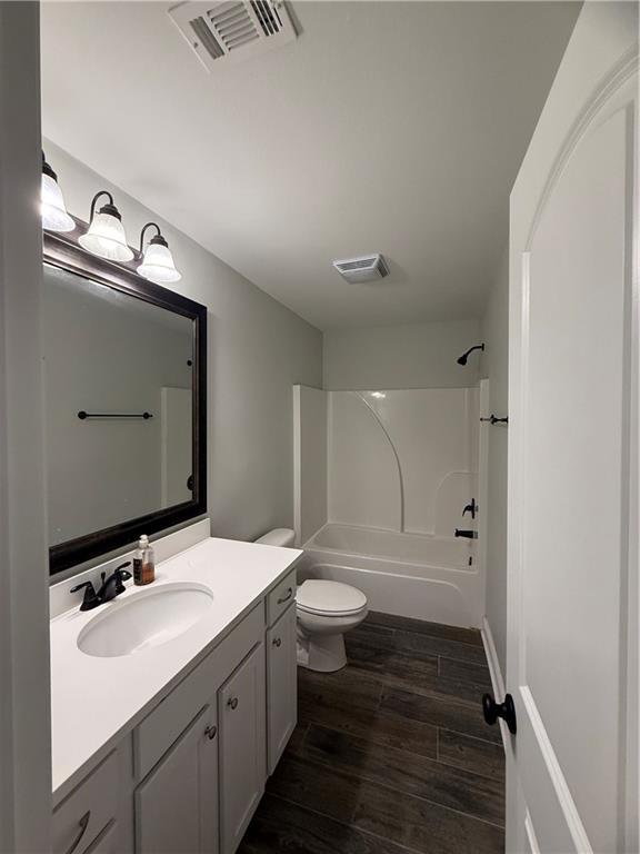 full bathroom with hardwood / wood-style floors, toilet, shower / tub combination, and vanity