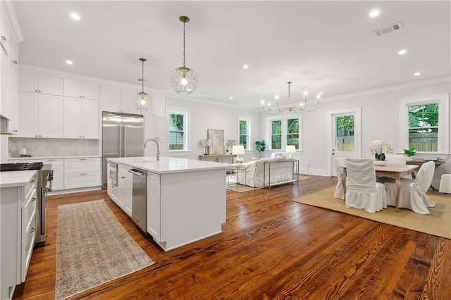 kitchen featuring white cabinets, hanging light fixtures, an island with sink, appliances with stainless steel finishes, and wood-type flooring