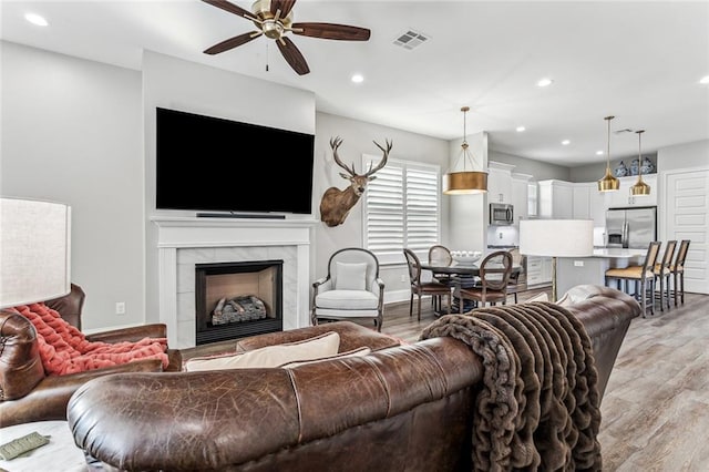 living room with hardwood / wood-style flooring, ceiling fan, and a high end fireplace