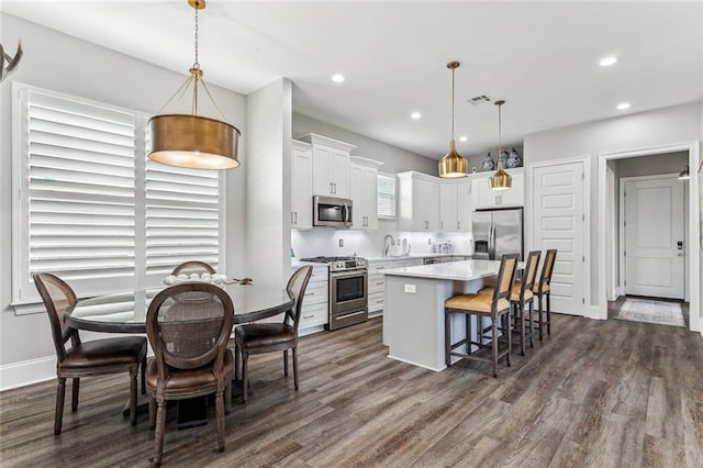 kitchen with pendant lighting, dark wood-type flooring, a kitchen island, white cabinetry, and stainless steel appliances