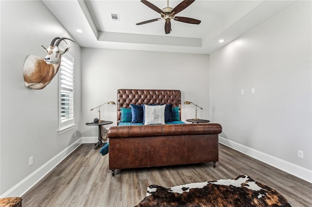 bedroom with wood-type flooring, a tray ceiling, and ceiling fan