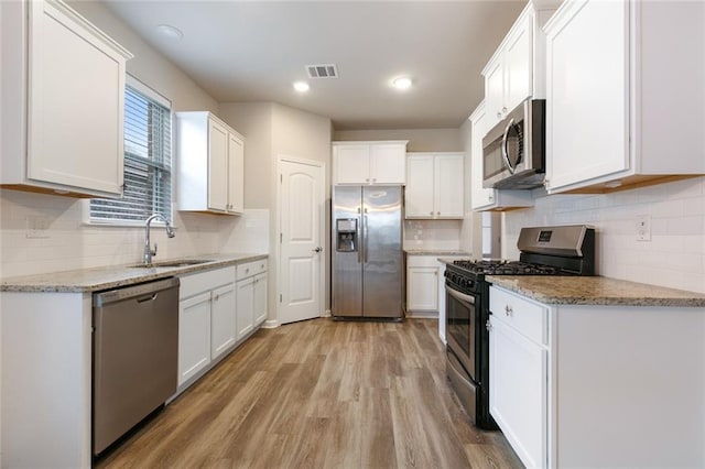 kitchen featuring stainless steel appliances, white cabinetry, light hardwood / wood-style floors, and sink