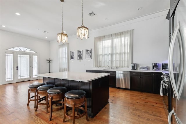 kitchen with a center island, a kitchen breakfast bar, hanging light fixtures, ornamental molding, and stainless steel appliances