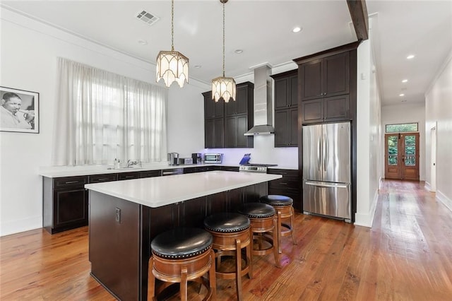 kitchen featuring stainless steel appliances, wall chimney range hood, a kitchen breakfast bar, decorative light fixtures, and a kitchen island