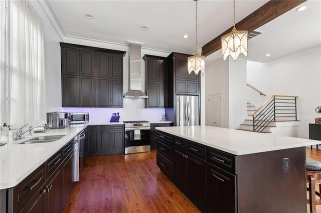 kitchen with wall chimney exhaust hood, beamed ceiling, decorative light fixtures, a kitchen island, and appliances with stainless steel finishes