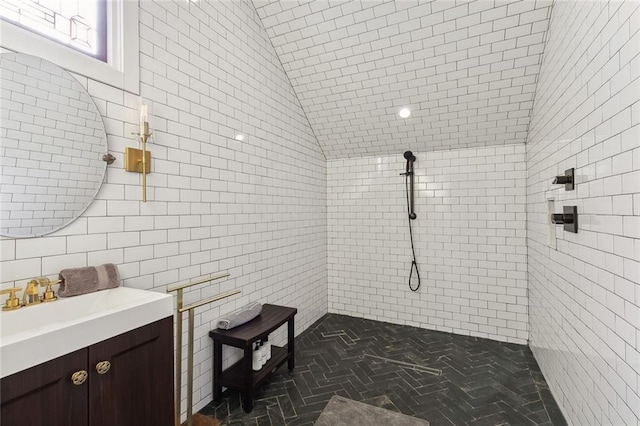 bathroom with a tile shower, vanity, and tile walls