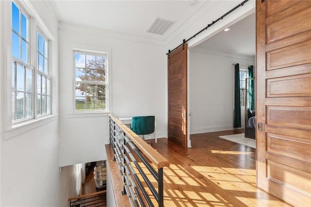 corridor with a barn door, crown molding, and hardwood / wood-style floors