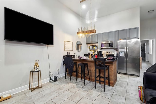 kitchen with stainless steel appliances, a high ceiling, a kitchen bar, gray cabinets, and light tile patterned floors