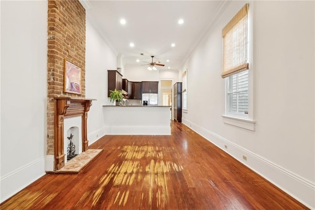 unfurnished living room featuring crown molding, a large fireplace, ceiling fan, and wood-type flooring