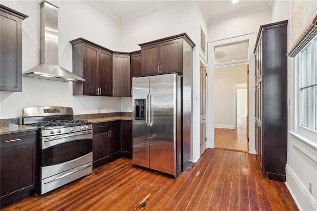 kitchen with dark wood-type flooring, stainless steel appliances, wall chimney range hood, stone countertops, and ornamental molding