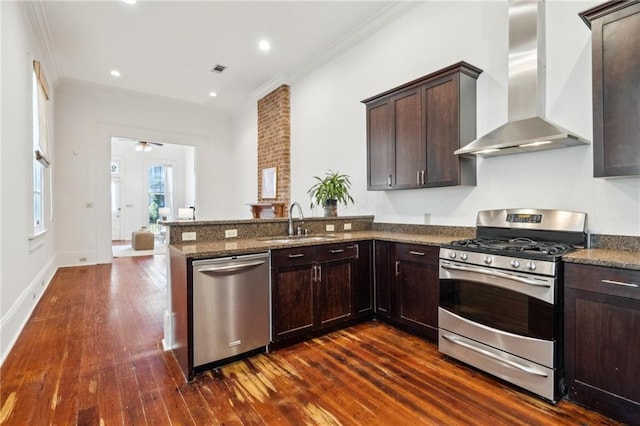 kitchen with kitchen peninsula, stainless steel appliances, dark wood-type flooring, sink, and wall chimney range hood