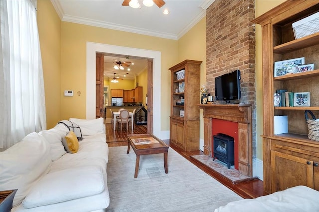 living room with hardwood / wood-style floors, a wood stove, ceiling fan, and ornamental molding