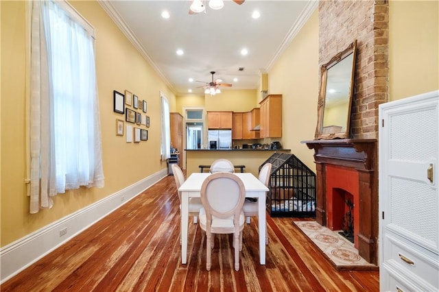 dining room with hardwood / wood-style flooring, ceiling fan, ornamental molding, and a fireplace