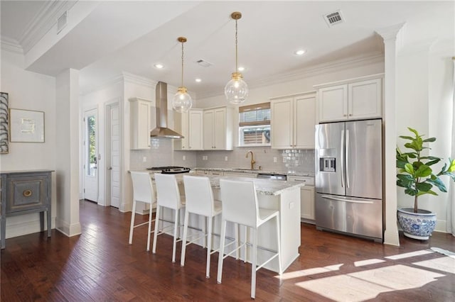 kitchen with a center island, sink, stainless steel appliances, wall chimney range hood, and pendant lighting