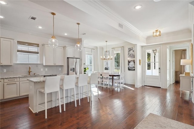 kitchen featuring light stone countertops, stainless steel fridge, decorative backsplash, decorative light fixtures, and a center island