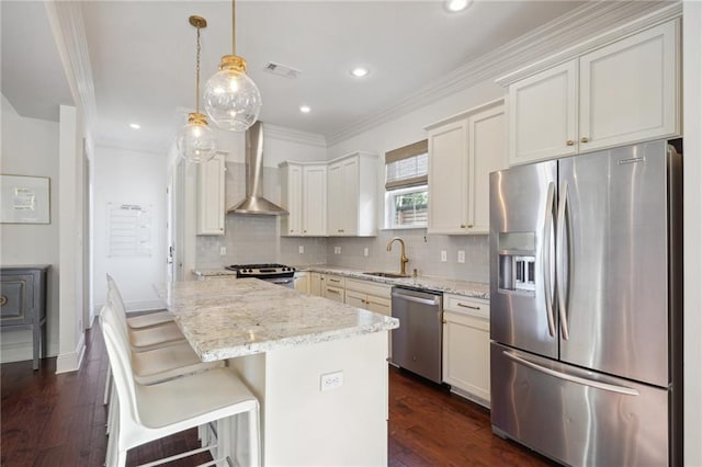 kitchen with appliances with stainless steel finishes, light stone counters, wall chimney exhaust hood, decorative light fixtures, and a center island