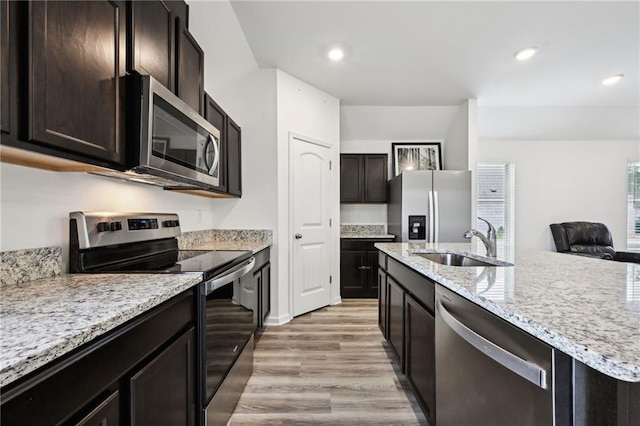 kitchen featuring light stone countertops, stainless steel appliances, a kitchen island with sink, sink, and light hardwood / wood-style flooring