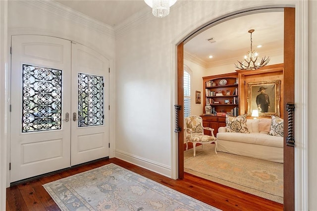 entrance foyer with a notable chandelier, ornamental molding, and dark wood-type flooring