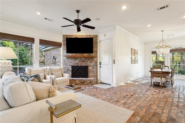 living room with ceiling fan with notable chandelier, a brick fireplace, and crown molding