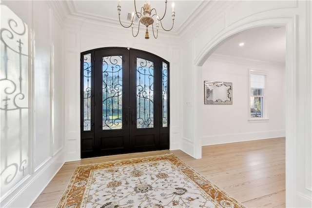 foyer entrance featuring light hardwood / wood-style floors, french doors, a chandelier, and ornamental molding