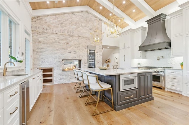 kitchen featuring decorative backsplash, custom exhaust hood, sink, hanging light fixtures, and an island with sink