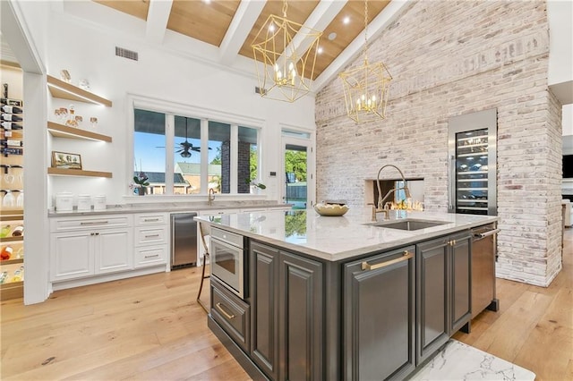 kitchen featuring light stone countertops, a kitchen island with sink, beamed ceiling, a high ceiling, and white cabinetry