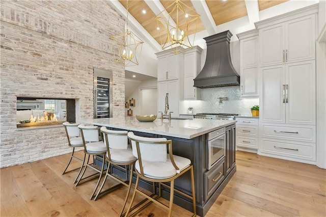 kitchen with beam ceiling, a kitchen bar, premium range hood, and hanging light fixtures