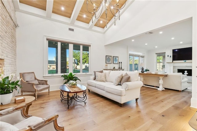 living room featuring beamed ceiling, a notable chandelier, light wood-type flooring, and a towering ceiling