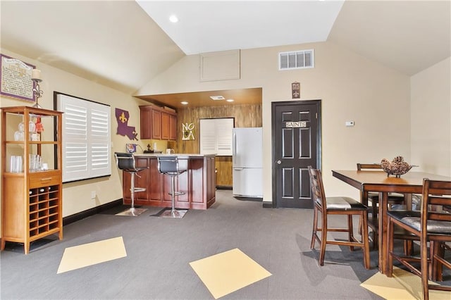 kitchen with dark carpet, lofted ceiling, white fridge, kitchen peninsula, and a breakfast bar area