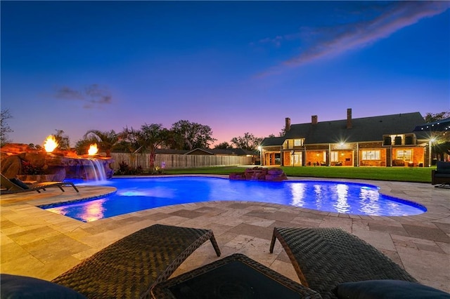 pool at dusk with a jacuzzi, pool water feature, a patio, and a lawn