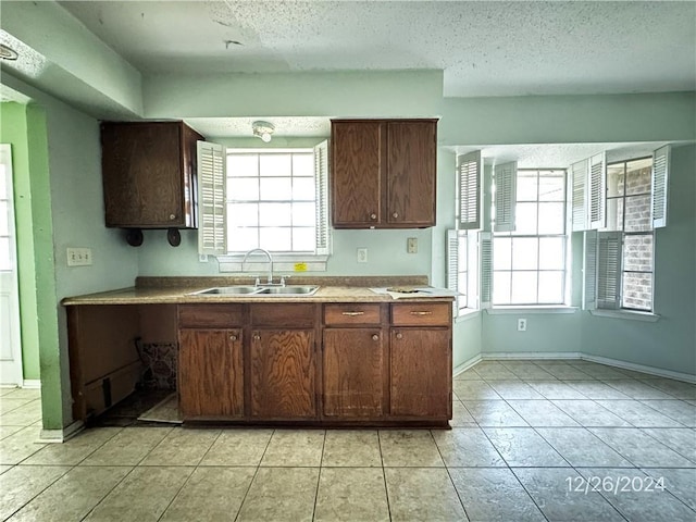 kitchen featuring dark brown cabinetry, sink, light tile patterned flooring, and a textured ceiling