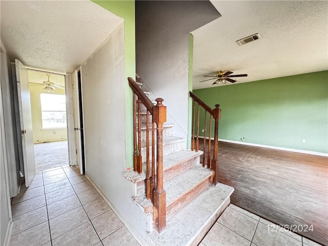 staircase featuring ceiling fan, tile patterned flooring, and a textured ceiling