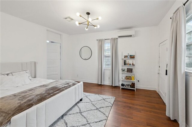 bedroom with a wall unit AC, dark wood-type flooring, and a notable chandelier