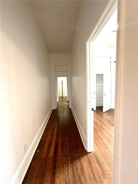 corridor featuring a textured ceiling, baseboards, and dark wood-style flooring