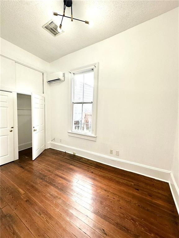 unfurnished bedroom with dark wood-style floors, baseboards, a textured ceiling, and a wall mounted air conditioner