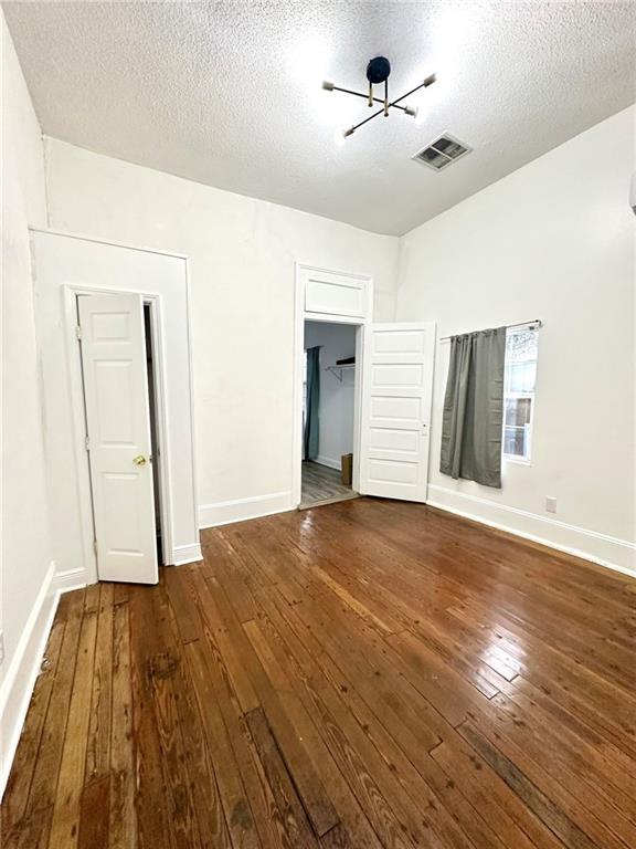 spare room featuring a textured ceiling, wood finished floors, visible vents, and baseboards