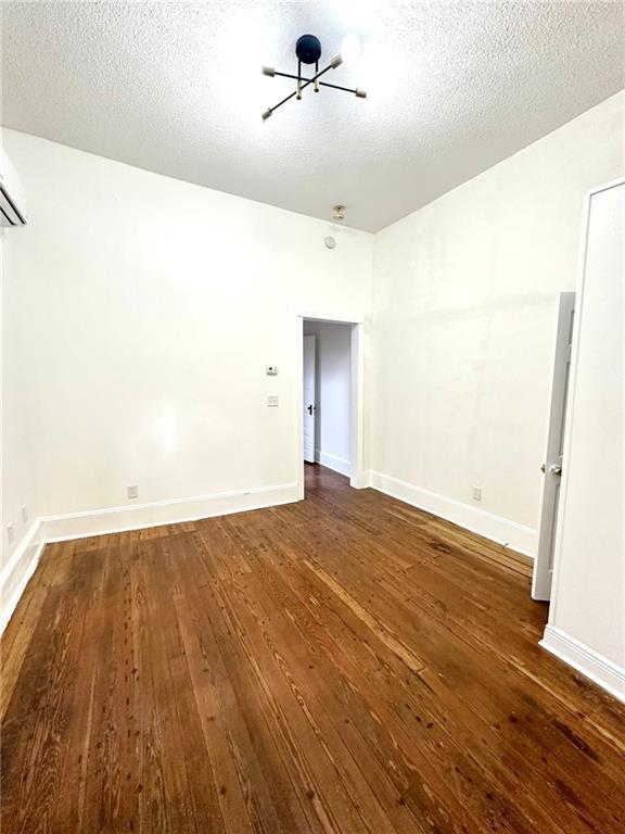 empty room featuring a notable chandelier, baseboards, dark wood finished floors, and a textured ceiling