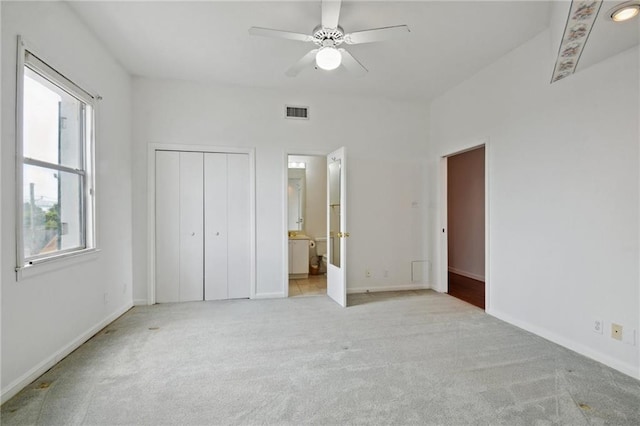 unfurnished bedroom featuring ceiling fan, light colored carpet, connected bathroom, and multiple windows