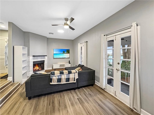 living room featuring ceiling fan, light wood-type flooring, a tile fireplace, and french doors